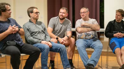 Pět účastníků sedí v půlkruhu a povídá si před ostatními.